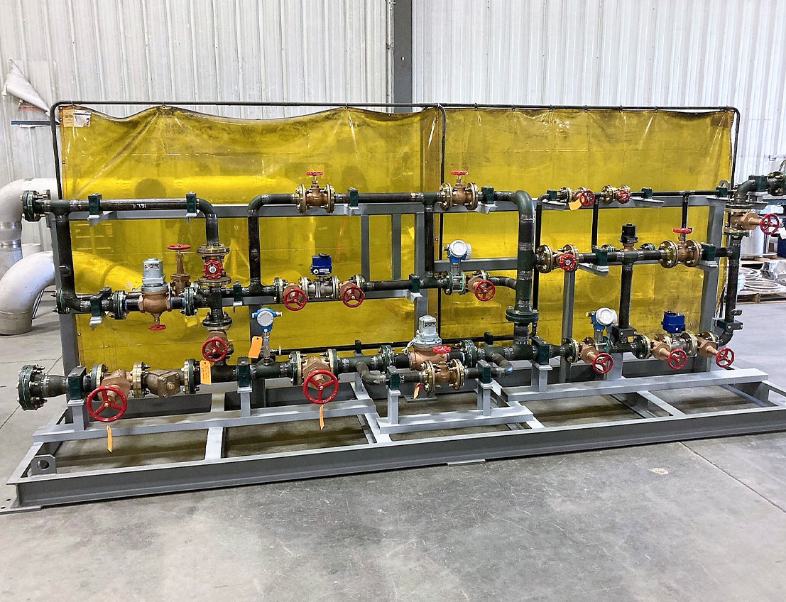 Custom carbon steel piping skid made exactly to client specs, featuring valves, controls, gauges, bypasses, and filters. Shown with yello backdrop and stainless steel frame