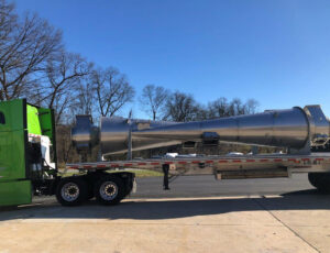 Custom fabricated uniform stainless steel finish cyclones loaded on a semi truck in front of a blue sky with trees.