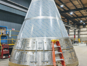 The bottom of a grey cyclone of a large metal spray dryer, which is shown inverted and in the process of placing stainless steel sheet metal over the sculpted insulation.