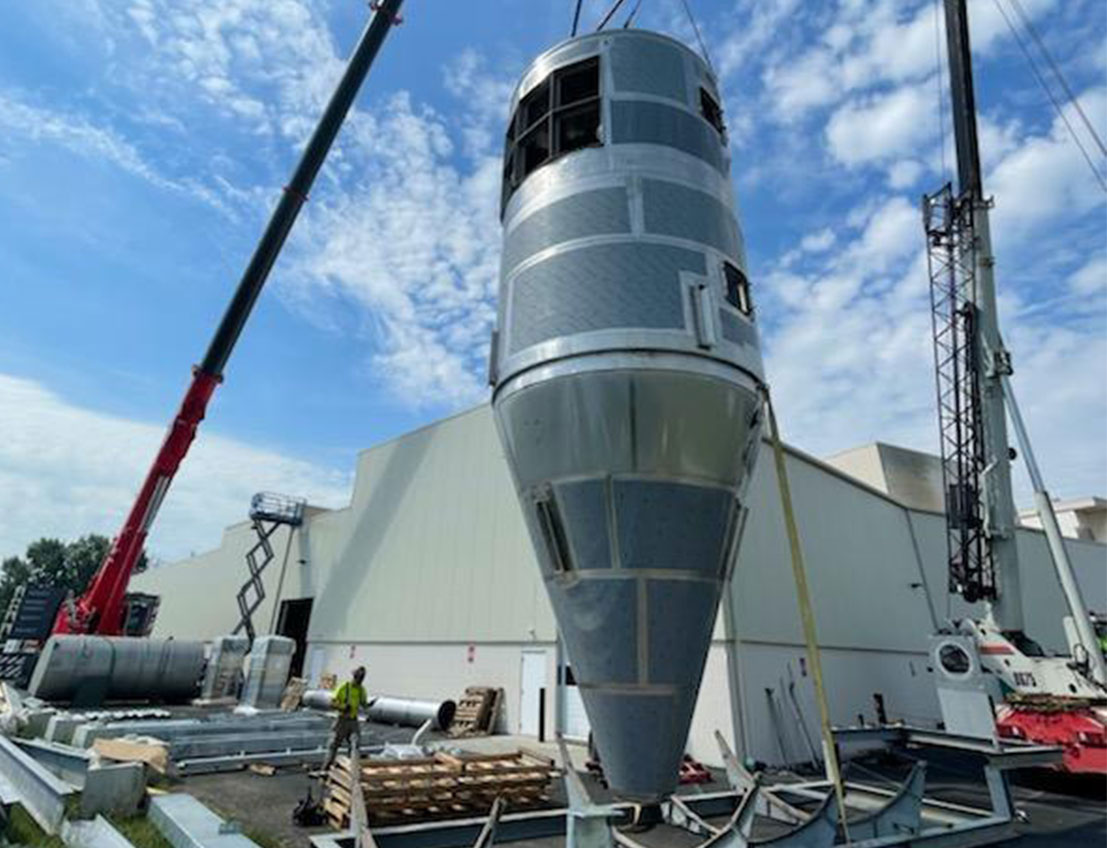 Gray Finished spray dryer being lifted into place for installation at a food and beverage facility pictured against a blue sky with clouds