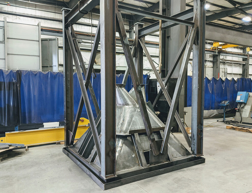 Carbon Steel Dual Chute Hopper, dark grey steel frame upside down on grey cement