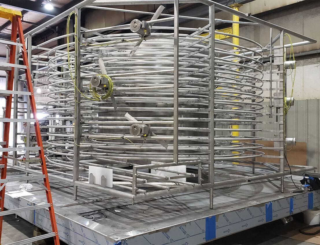 Food-grade spiral freezer equipment under construction in our US facility, including sheet metal framing, bent sheet metal, spiral tubes, plumbing, and wiring.