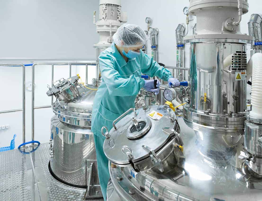 Technician in blue sanitary suit working on medical and pharmaceutical equipment in a lab