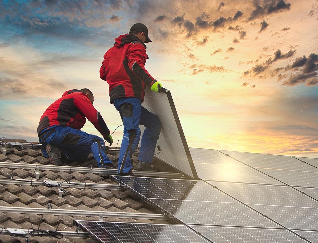 Two environmental industrial contractors installing solar panels on roof during the sunset