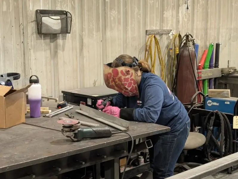 Woman welder wearing a tan welding helmet with pink cheetah print works at SWF.