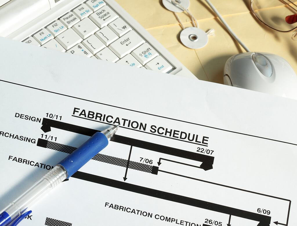 Image of a document sitting on a desktop, labeled "fabrication schedule" with a blue ink pen on top of it.