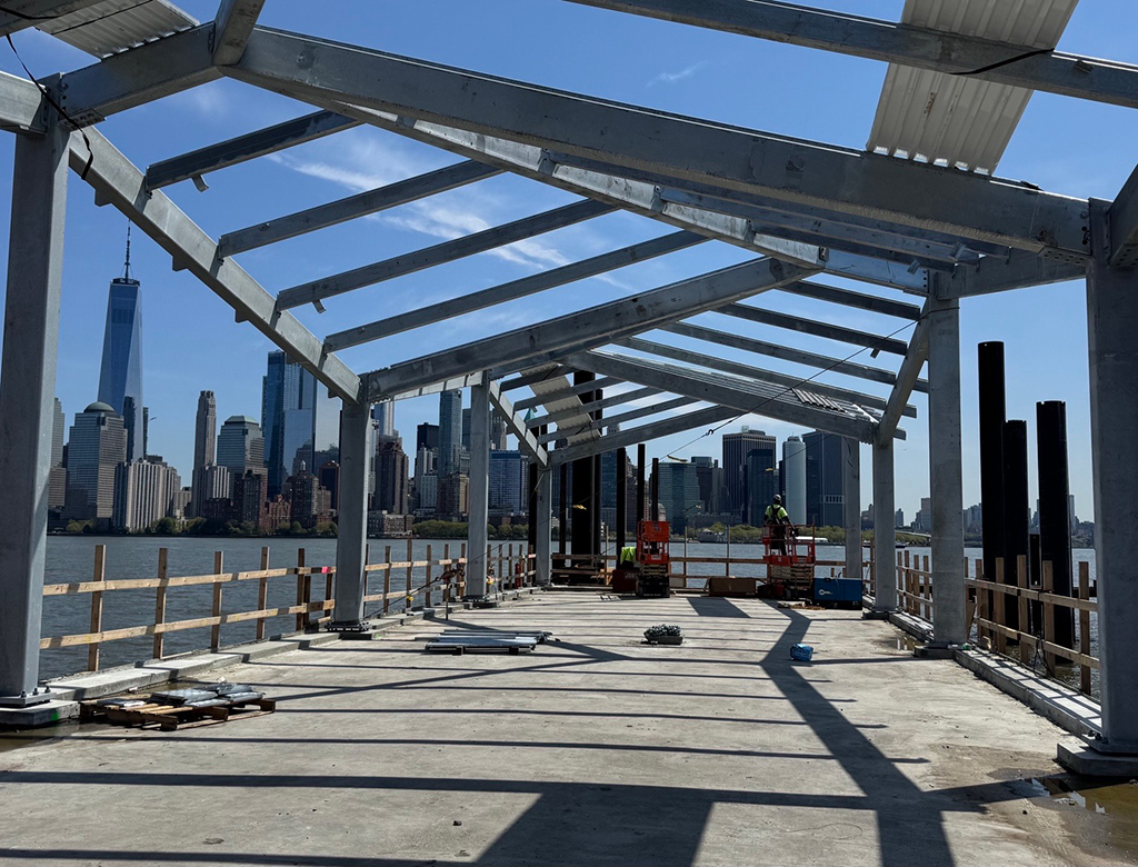 New York skyline visible behind the structural fabrication installation of a beautifully designed steel canopy.